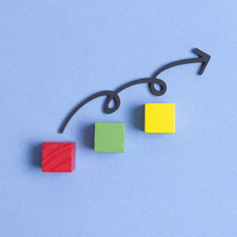 Continu verbeteren met Lean Six Sigma in kleine stapjes uitgelegd met drie houten blokjes met daarboven een pijl met krullen