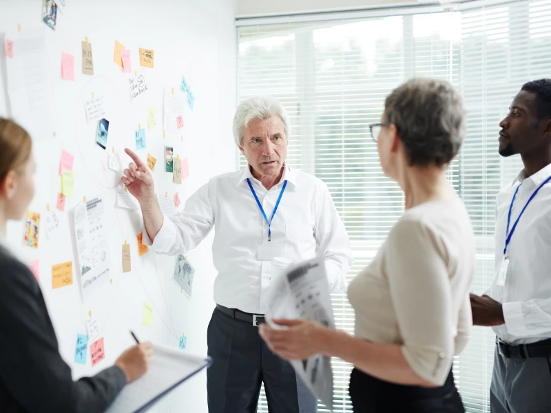Consultancy van Impactery in de Zorg sector, gevisualiseerd door een ervaren man die een whiteboard aanwijst tijdens een Lean Six Sigma workshop