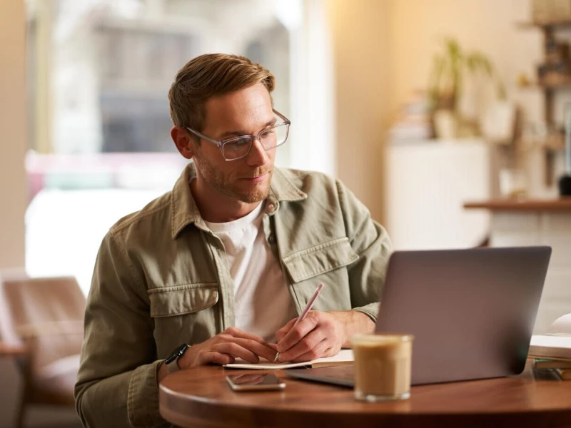 Deelnemer maakt aantekeningen en kijkt aandachtig naar de laptop waarop hij een online Lean Six Sigma cursus volgt bij Impactery