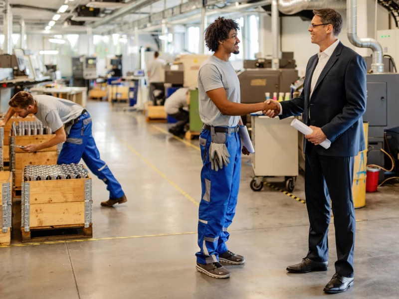 Een leidinggevende schud de hand van een arbeider, waarmee het Go Gemba principe wordt geillustreerd door naar de werkvloer te gaan