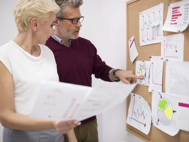 Een man en vrouw die naar een bord kijken en wijzen naar een OEE berekening grafiek.