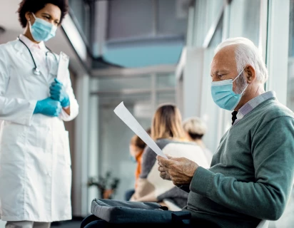 Een arts met mondkapje op die een document overhandigt aan een patient met mondkapje op, typerend voor de Zorg sector